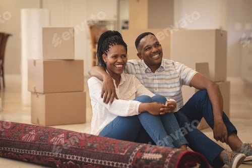Preview: Front view of happy African American couple sitting on floor and looking away at home