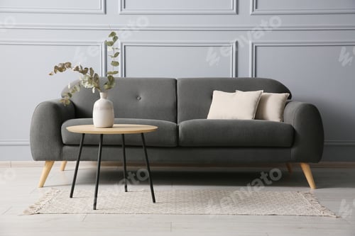 Preview: Stylish sofa with cushions and eucalyptus branches in vase on coffee table in room