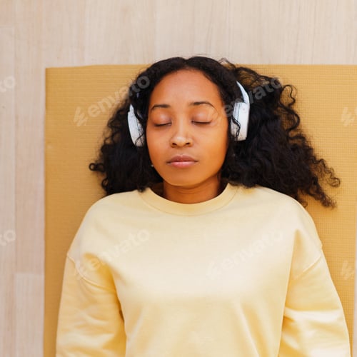 Preview: African-American woman in headphones having rest on mat with eyes closed. Relaxing after exercising