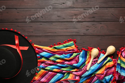 Preview: Mexican sombrero hat, maracas and colorful poncho on wooden background, flat lay. Space for text