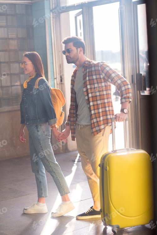 Preview: stylish couple of tourists in sunglasses with backpack and wheeled bag at subway