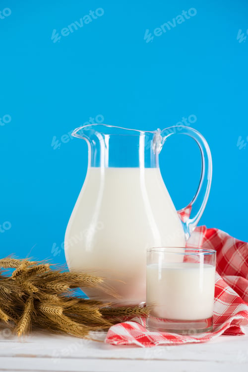 Preview: Close-up view of fresh organic milk in glass and jug with wheat ears on wooden table