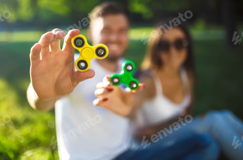 Preview: Young girl and boy playing with fidget spinners in the park. stress relieving toy. Sunny summer day.