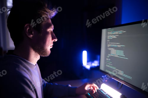 Preview: Focused Male Developer Coding Intently on a Computer in office at Night, looking at the screen