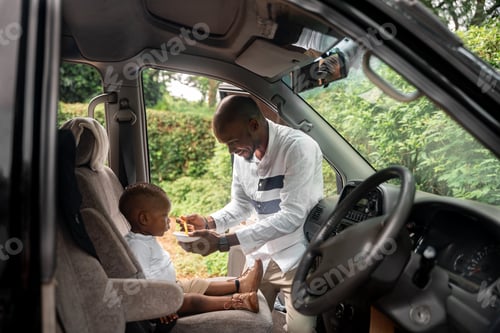 Preview: African american father feeding a baby boy inside a car