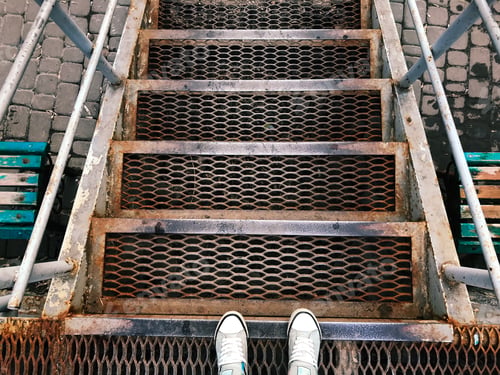 Preview: Feet in White Sneakers Standing on Metal Geometric Stairs