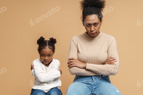 Preview: Displeased black mother and daughter frowning while sitting with arms crossed