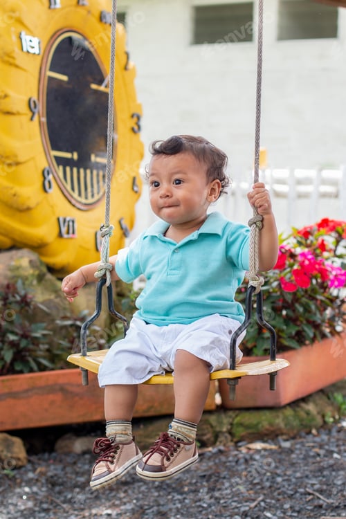 Preview: Vertical photo of cute baby riding on a swing in a colorful park.