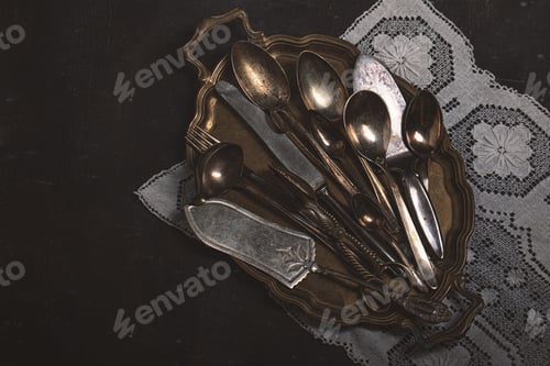 Preview: Old cutlery on a metal tray on a dark background in vintage style. Antiques.
