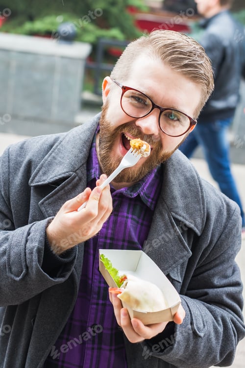 Preview: Fast food and meal concept - Young man eating take away food on the street