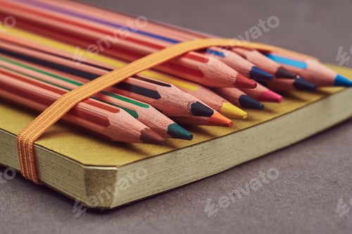 Preview: Multicolored pencils lying on a yellow notepad.