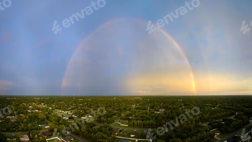 Preview: Colorful round rainbow over rural town suburbs against blue evening sky after heavy thunderstorm
