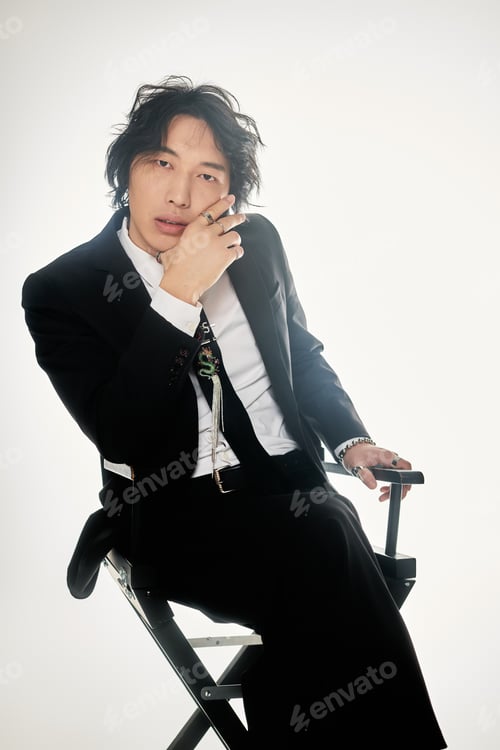 Preview: Young stylish Asian man exudes confidence while posing on a directors chair with a modern vibe
