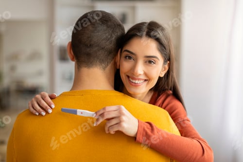 Preview: Expecting A Baby. Happy woman holding positive pregnancy test and hugging husband