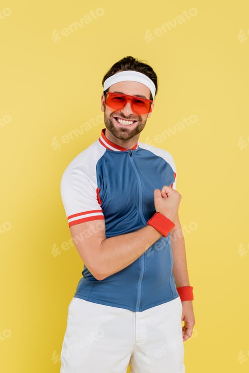 Preview: Positive sportsman in sunglasses showing muscles isolated on yellow