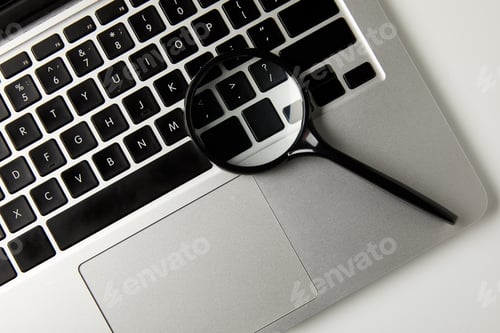 Preview: top view of magnifying glass and laptop on grey