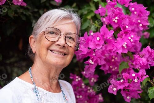 Preview: Outdoor close-up portrait of a smiling elderly woman near a pink bougainvillea flower plant in the p