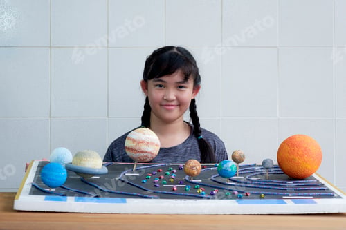 Preview: Young smiling Asian girl showing her homemade solar system model for science homework project