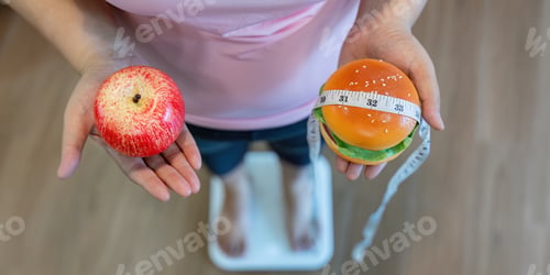 Preview: Overweight woman weighing choices, holding an apple and a burger with a measuring tape at home