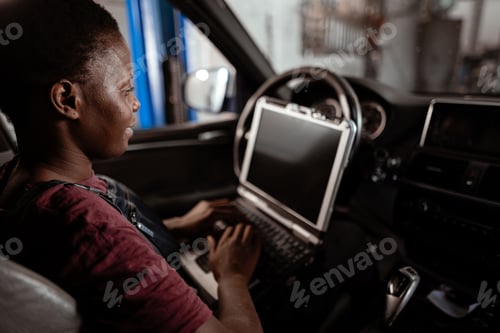 Preview: Young technician works on laptop inside a car in an automotive repair shop