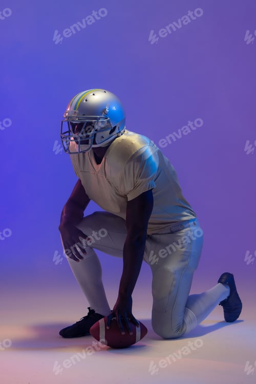 Preview: African american male american football player holding ball with neon blue lighting