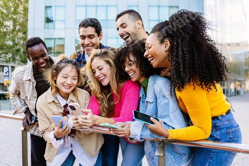 Preview: Young group of happy friends smiling while using mobile phone together outdoors