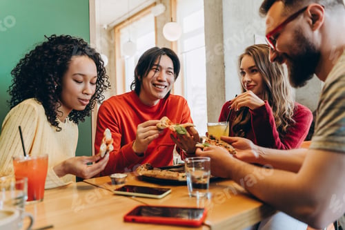Preview: Group of smiling cheerful friends enjoying pizza and drinks at restaurant table
