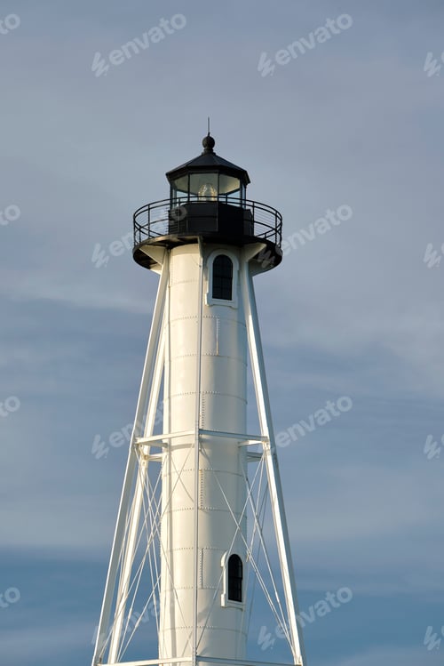 Preview: White tall lighthouse on sea shore against blue sky for commercial vessels navigation