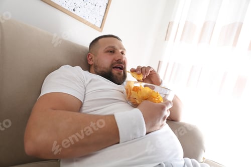 Preview: Lazy overweight man eating chips at home