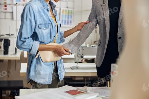 Preview: African-American dressmaker checks sleeve of new light grey jacket on mannequin in workshop