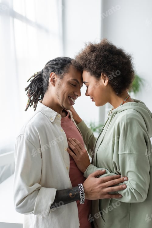Preview: Positive african american couple hugging with closed eyes at home