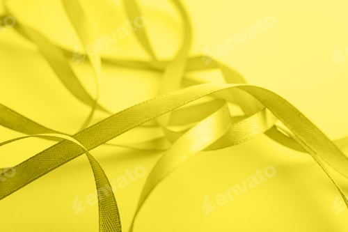 Preview: Curved yellow gold silk ribbon on yellow background. Closeup.