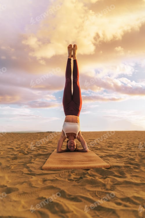 Preview: Beautiful woman practicing yoga on the beach at sunset, doing headstand exercise, salamba sirsasana