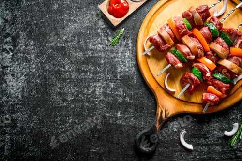Preview: Raw beef kebab with vegetables on a cutting Board with sauces, rosemary and onion slices.