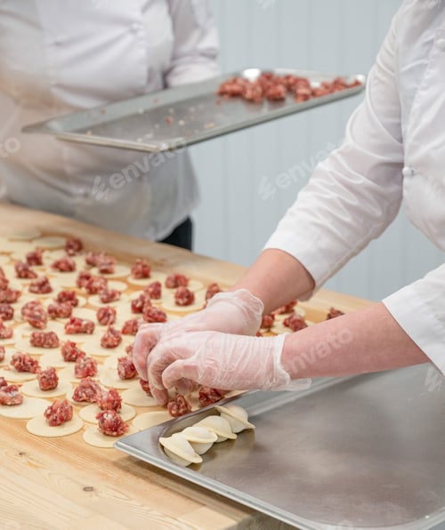 Preview: A workers handmade dumplings with raw meat filling on metal trays on a wooden table