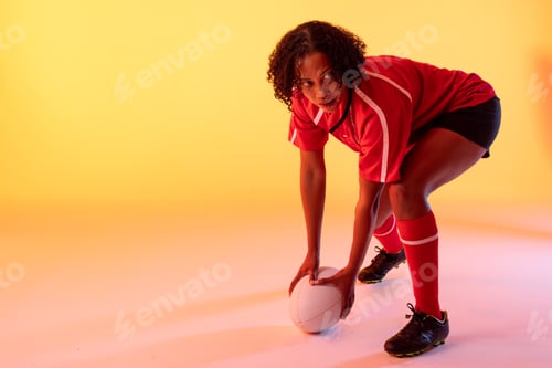 Preview: African american female rugby player with rugby ball over neon yellow lighting