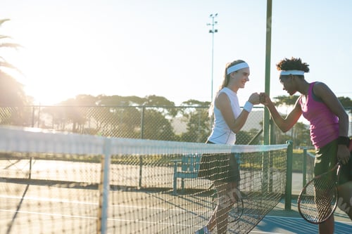 Preview: Happy multiracial young female tennis players giving fist bump over net at court