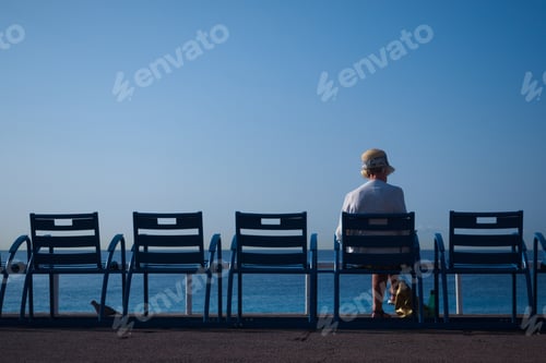 Preview: Closeup shot of a person sitting on a blue chair on the beach, a bird under one of the chairs