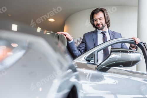 Preview: portrait of stylish businessman standing at new car at dealership salon