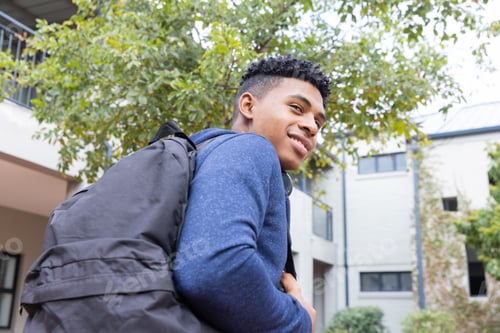 Preview: Carrying backpack and smiling, African American male student looking away outdoors at school