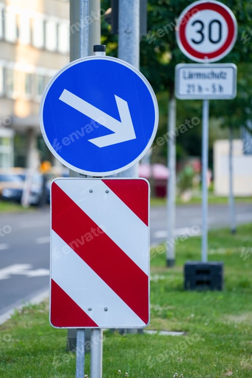Preview: Vertical closeup shot of a blue circular traffic sign with arrow pointing down and a blur background