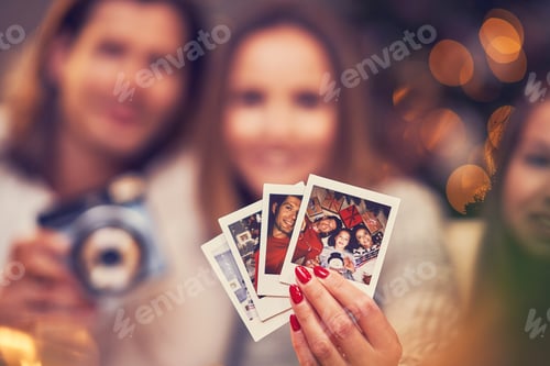 Preview: Beautiful couple celebrating Christmas at home and taking instant pictures