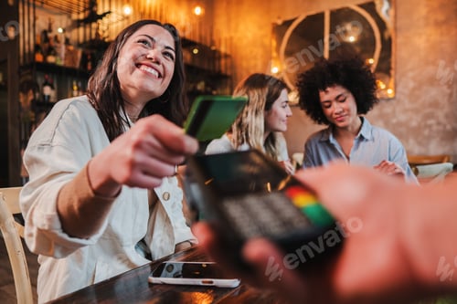 Preview: Happy young woman paying bill with a contactless credit card in a restaurant. Female smiling holding