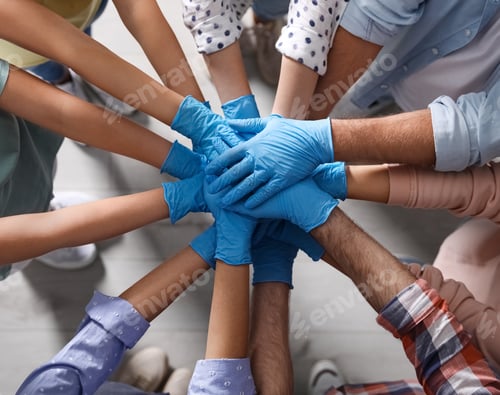 Preview: People in blue medical gloves stacking hands indoors, top view