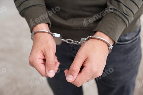Preview: Man in metal handcuffs on blurred background, closeup
