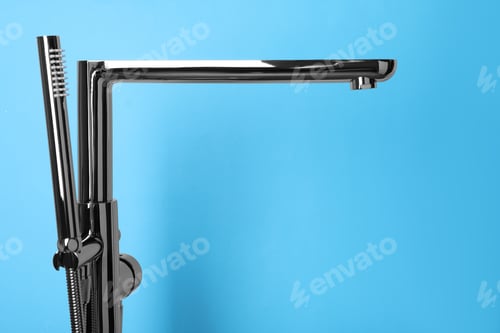 Preview: Modern bathtub faucet with hand shower on light blue background. Space for text