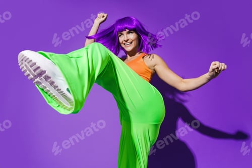 Preview: Carefree woman dancer wearing colorful sportswear having fun against purple background
