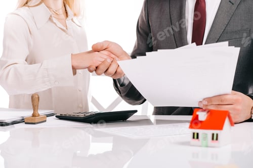 Preview: cropped view of businessman and businesswoman shaking hands and holding papers isolated on white,