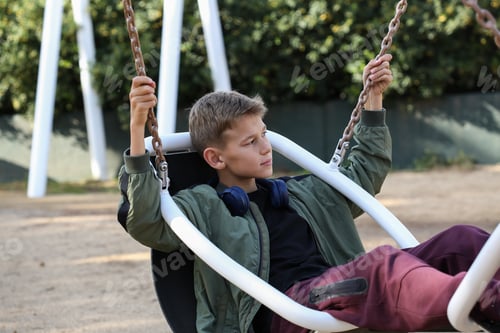 Preview: Handsome teenager sitting in a swing and relaxing. Adolescent discovers city streets