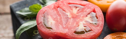 Preview: panoramic shot of sliced red and yellow tomatoes with spinach on black tray on wooden table